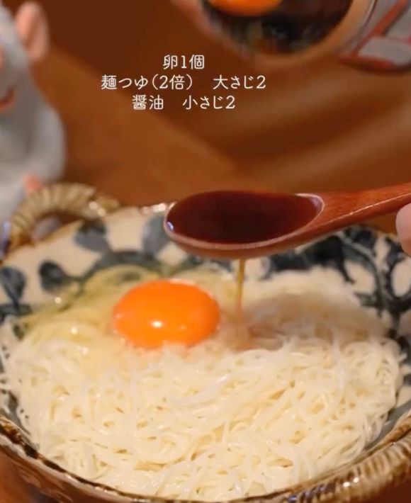 卵を割り入れたそうめんに醤油などの調味料をかける様子