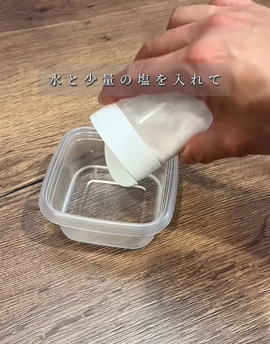 水を入れたプラスチック製保存容器に塩を入れる様子