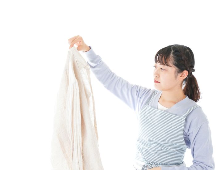 エプロンを着けた女性が嫌そうな顔でワイシャツを持っている写真