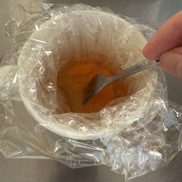ラップを敷いたマグカップに入れた卵と調味料をフォークでかき混ぜる様子