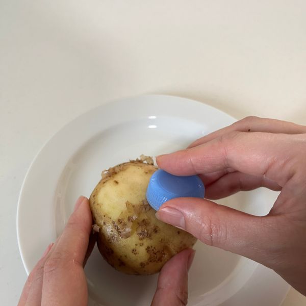 ペットボトルのキャップでジャガイモの皮をこする様子