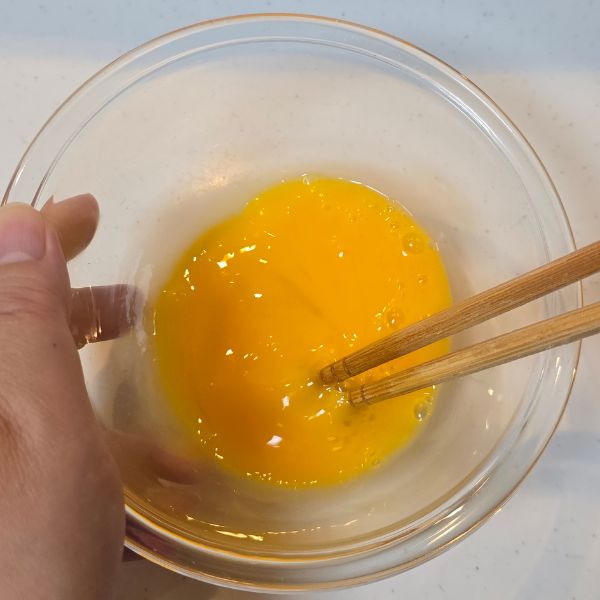 ボウルに割り入れた卵を箸で溶きほぐす様子