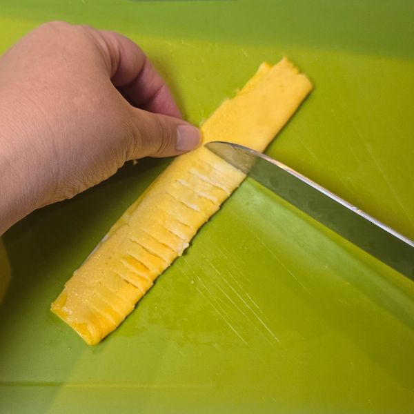 縦半分にした薄焼き卵を半分に折って包丁で切り目を入れる様子
