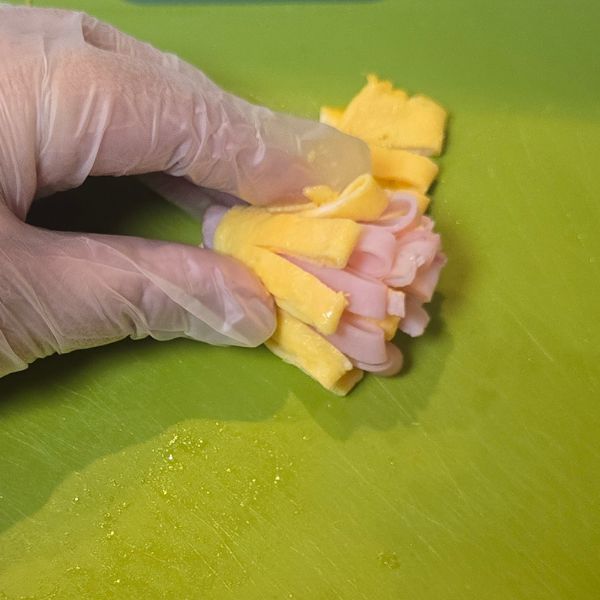 切り目を入れた薄焼き卵とハムを重ねて巻く様子