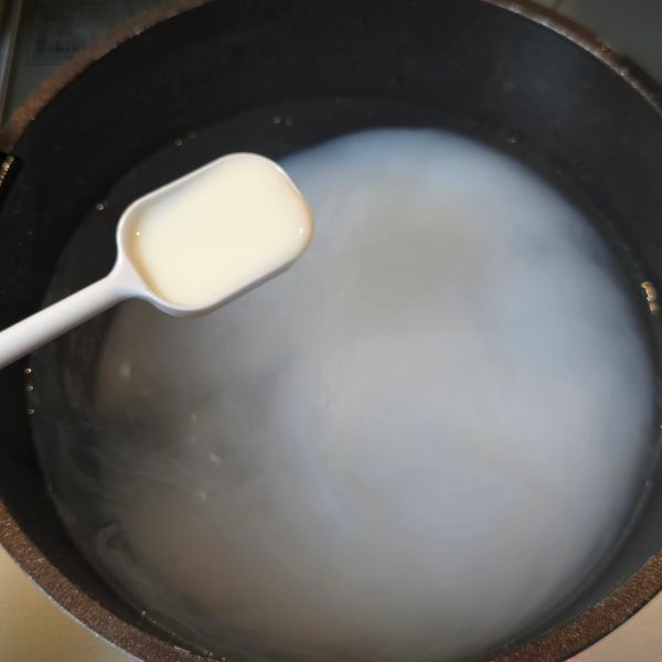 水の入った鍋に計量スプーンで牛乳を入れる様子