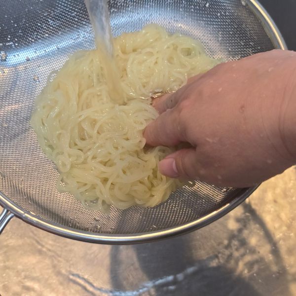 ゆでた麺をザルにあげて流水で洗う様子