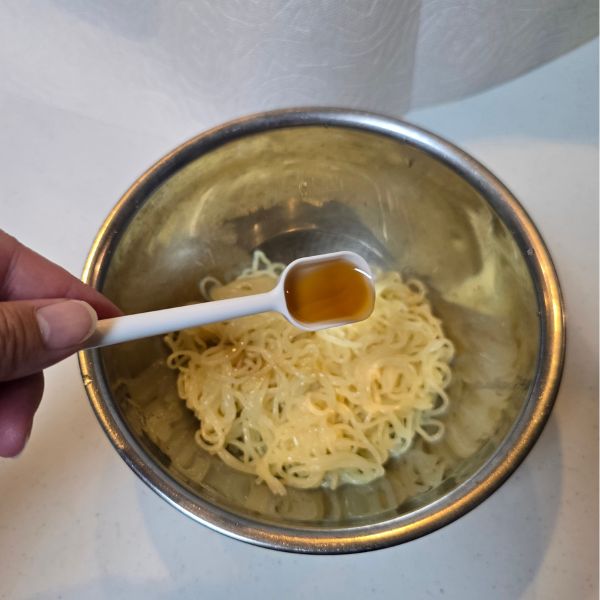 ボウルに水気を切った麺を入れてごま油をかける様子