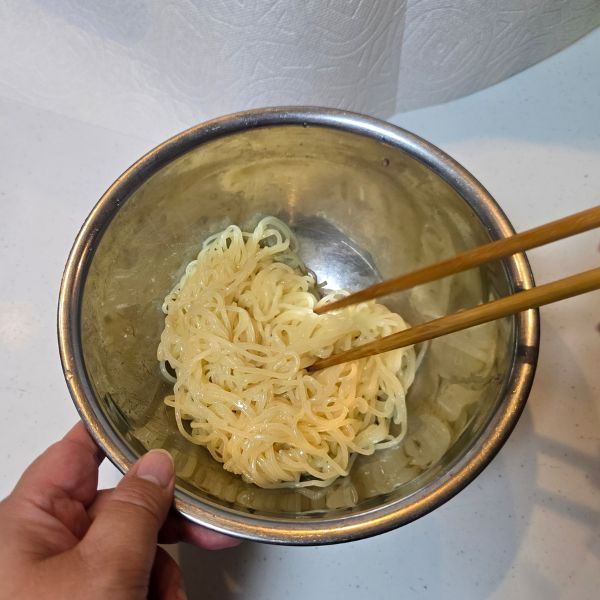 ごま油をかけた麺を菜箸でほぐす様子