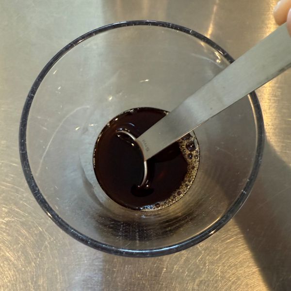 グラスに入った麦茶に砂糖を入れて計量スプーンで混ぜる様子