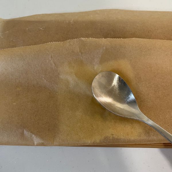 加熱したスライスチーズをクッキングシートで挟んでスプーンで砕く様子