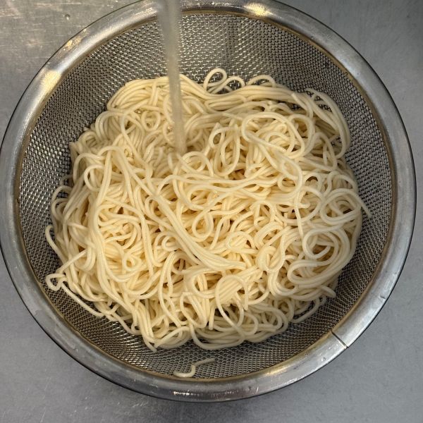 ゆで上がったそうめんをザルにあげて流水をかける様子