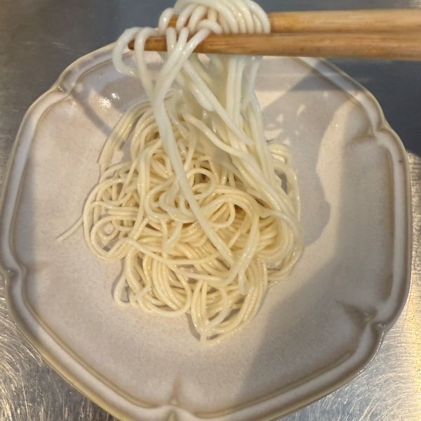 小皿にのせたそうめんを箸でつまみ上げた様子