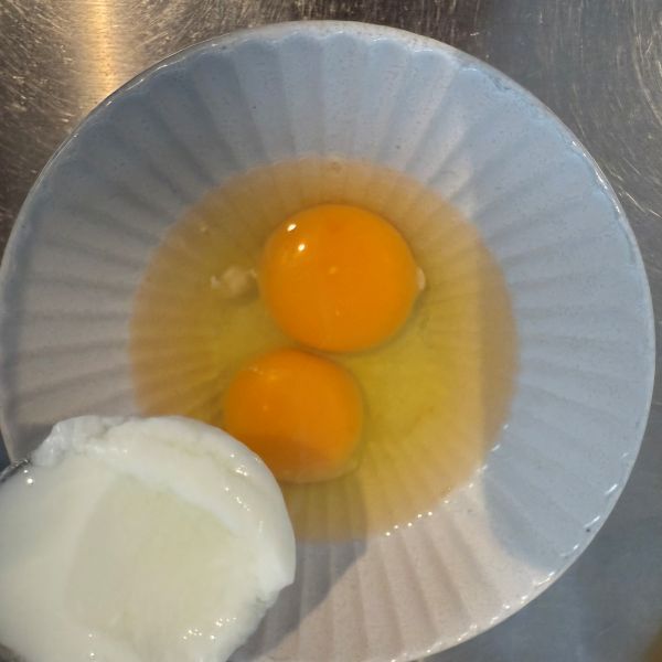 卵を割り入れた皿にヨーグルトを入れる様子