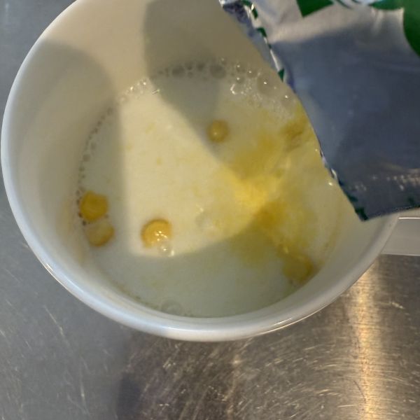 牛乳の入ったマグカップに粉末のコーンスープを入れる様子