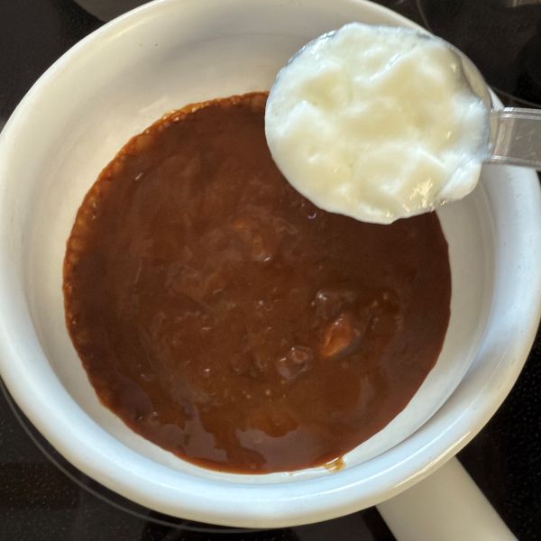 鍋に入っているカレーに大さじ1杯のヨーグルトを入れる様子