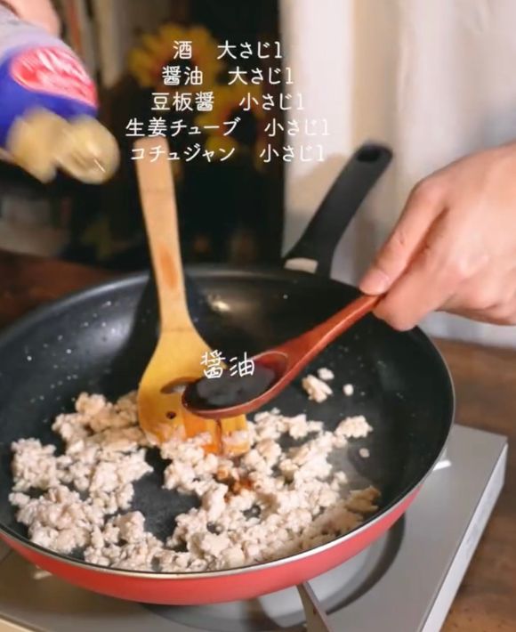 鶏ひき肉を炒めているフライパンに醤油を加える様子