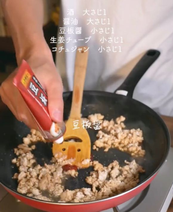 鶏ひき肉を炒めているフライパンに豆板醤を入れる様子