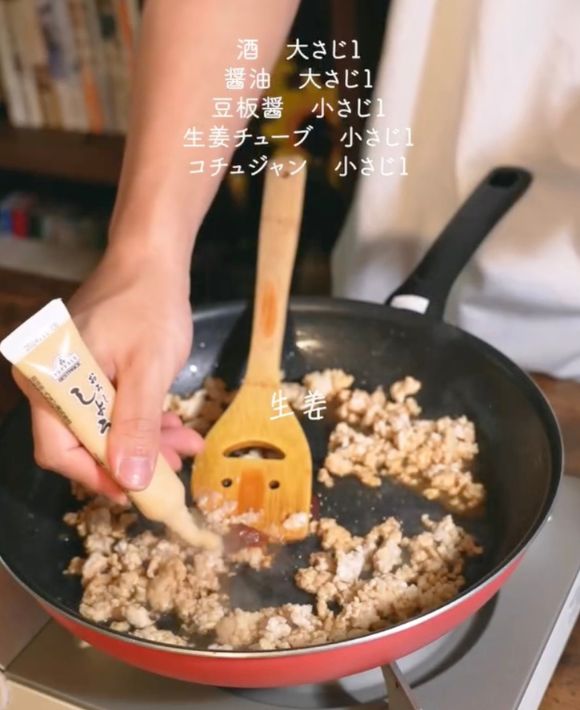 鶏ひき肉を炒めているフライパンにチューブに入ったショウガを入れる様子