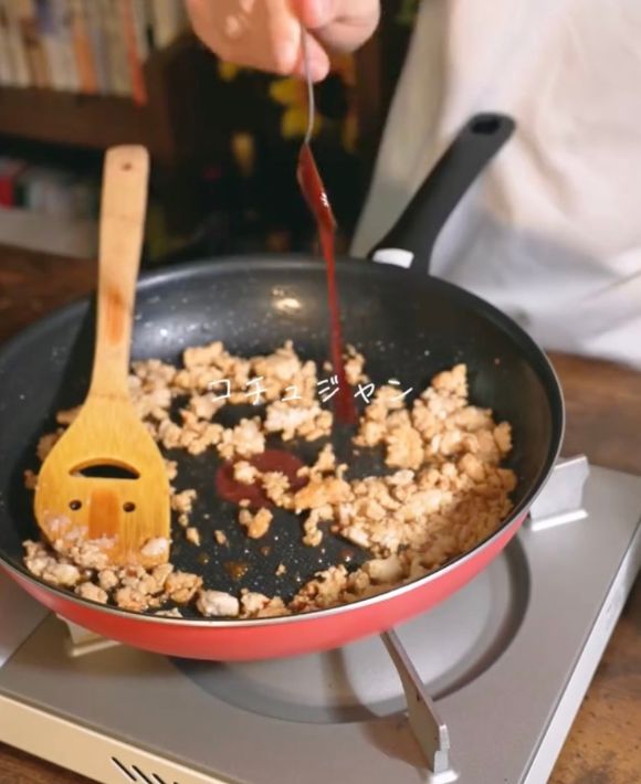 鶏ひき肉を炒めているフライパンにスプーンでコチュジャンを入れる様子