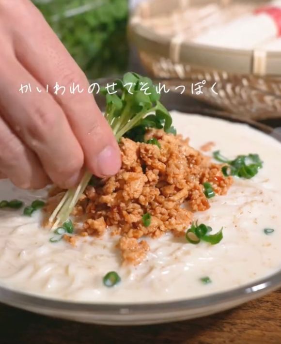 豆乳スープをかけたそうめんにかいわれ大根と小口切りにしたネギをのせる様子