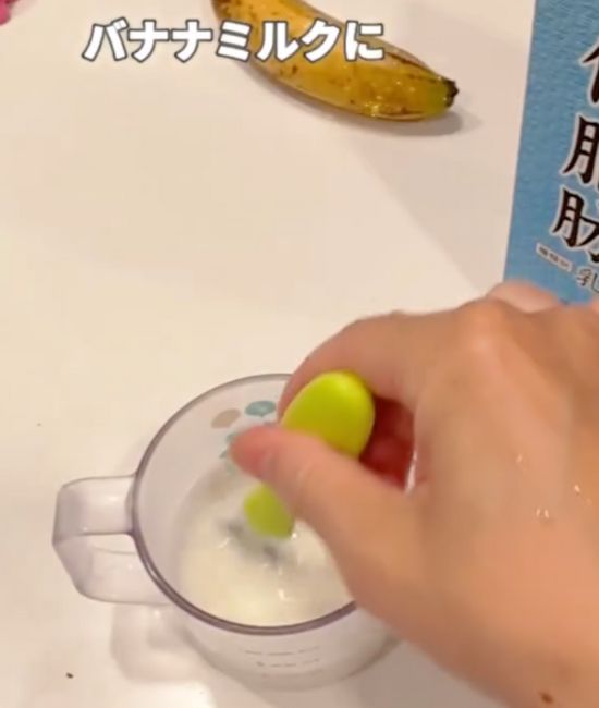 牛乳を入れたグラスに冷凍したバナナを割り入れてかき混ぜる様子