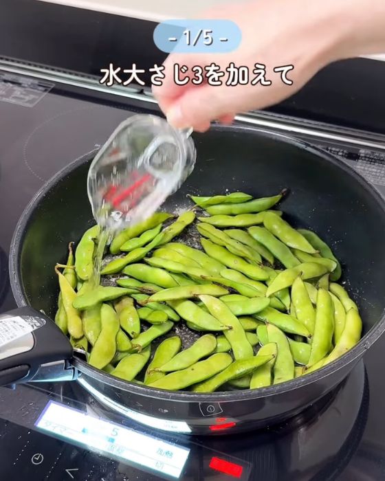 枝豆を焼いているフライパンに計量カップで水を入れる様子