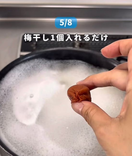 そうめんをゆでている鍋に梅干しを入れようとしている様子