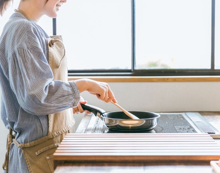 エプロンを着けた女性がフライパンを持って調理をしている様子