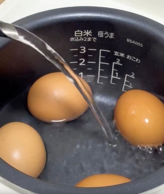 生卵を4つ入れた炊飯釜にお湯を注ぐ様子