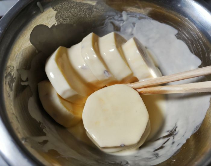 切ったサツマイモに天ぷらの衣をつける様子