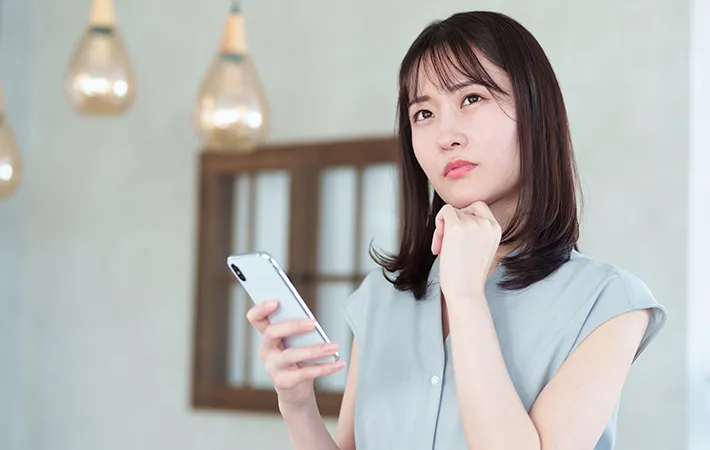スマホをもって悩む女性の写真