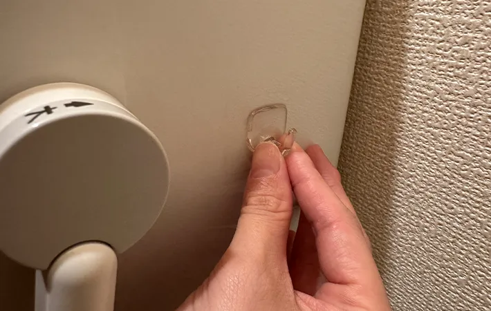 『何度でも貼ってはがせるフィルムフック 固定タイプ 小』をトイレタンクに吸着させる画像（撮影：grape編集部）