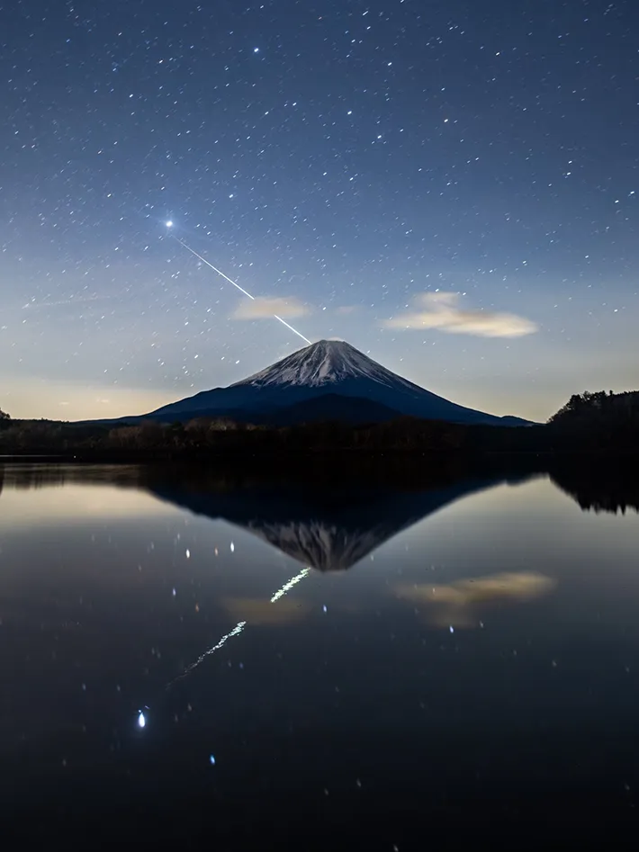 ふたご座流星群の流星が突き刺さったように見える富士山の写真
