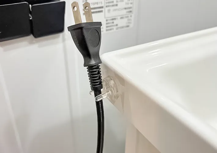 『貼ってはがせるフィルムフック歯ブラシホルダー』とドライヤーのプラグの写真（撮影：キジカク）