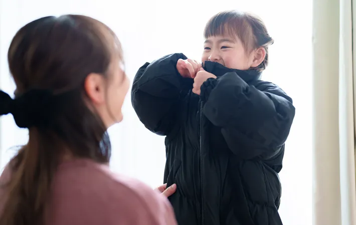 『娘が服を着るのを手伝う母親』の写真