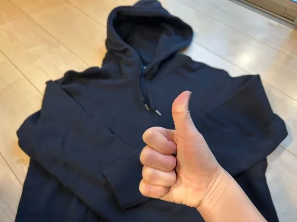 床に置かれた黒いパーカーを背景にサムズアップしている様子