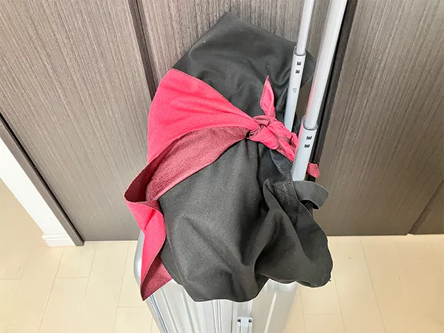 風呂敷の角をキャリーケースの持ち手に通し、上にカバンを置いて結ぶ（撮影：grapeライフハック編集部）