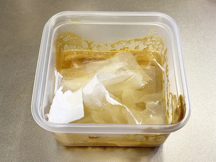 水と洗剤が入った汚れたプラ容器に、ちぎったキッチンペーパーを浮かべている画像（撮影：grapeライフハック編集部）