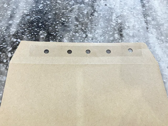 封筒に穴開けパンチで穴を開け、セロハンテープを貼った場面（撮影：grapeライフハック編集部）