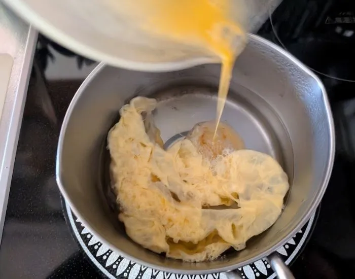 スープに卵液を円を描くように注いでいる様子（撮影：grapeフード編集部）