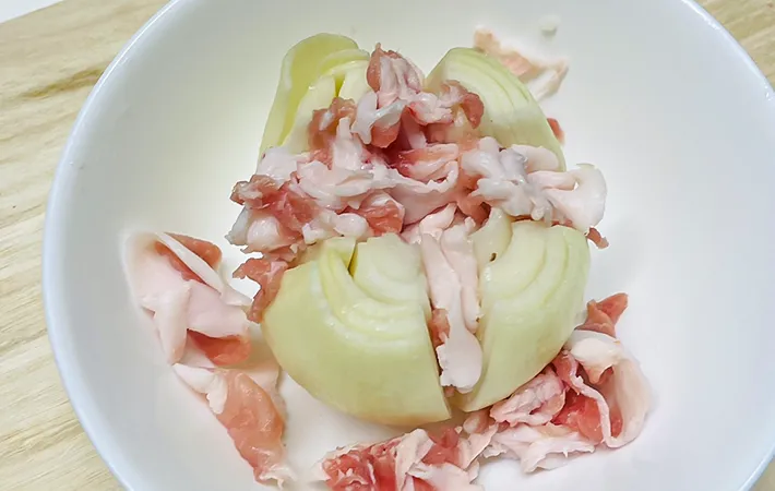 豚肉をタマネギに挟む写真