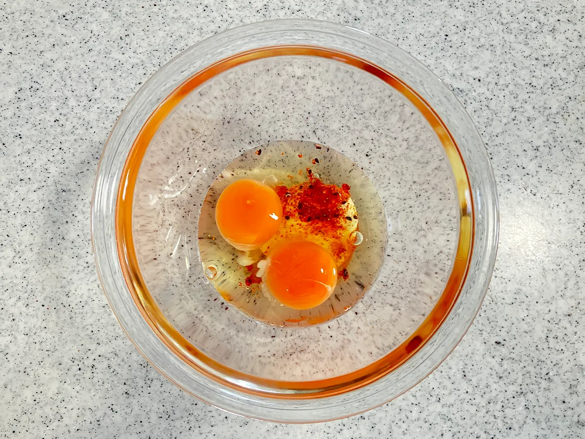 マヨネーズ、ラー油、七味唐辛子を入れて、卵を割り入れた場面(撮影:grapeフード編集部)