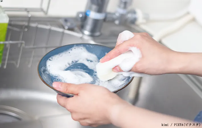 洗剤をつけたスポンジで食器洗いをする写真