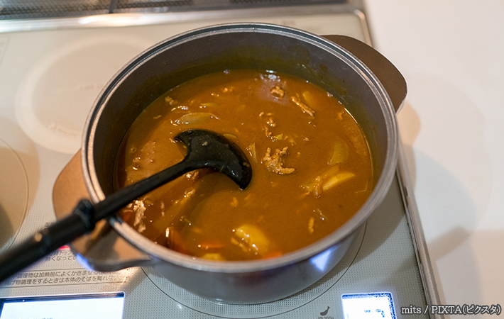 鍋で大量に料理したカレーをおたまでかき混ぜている写真