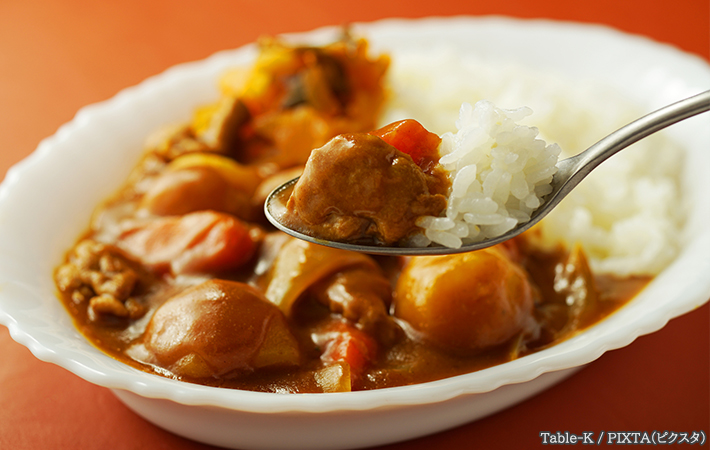 白い皿に取り分けたカレーをスプーンですくっている写真