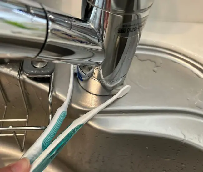 歯ブラシで蛇口の根元を挟んで掃除している様子（撮影：grapeライフハック編集部）