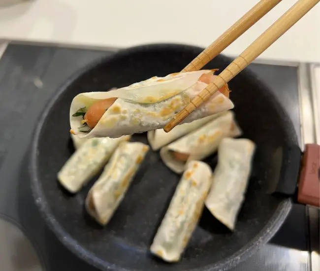 フライパンで餃子の皮巻きソーセージを焼いている様子（撮影：grapeフード編集部）