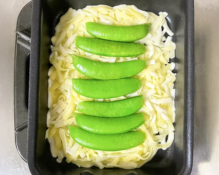 玉子焼き器にシュレッドチーズとスナップエンドウを重ねる写真（撮影：grapeフード編集部）