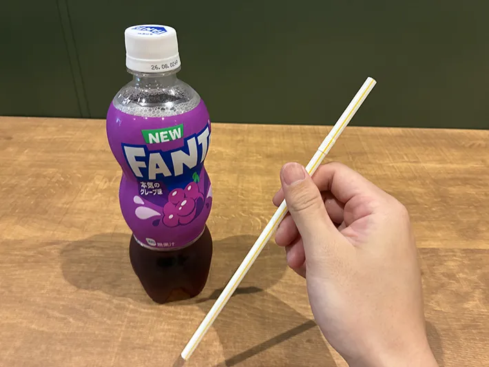 机に置かれたペットボトル飲料と、指でつかんだストロー（撮影：grapeライフハック編集部）