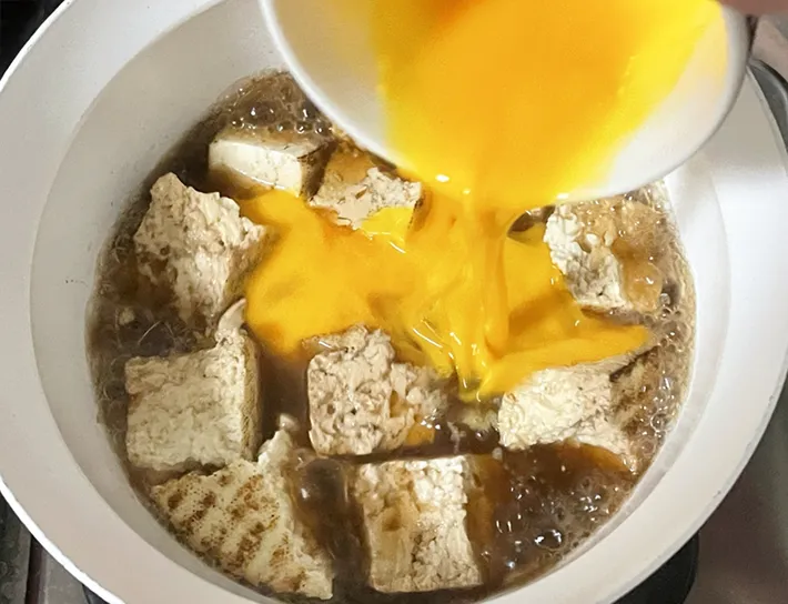焼き豆腐を煮込む鍋に溶き卵を入れる写真（撮影：grapeフード編集部）